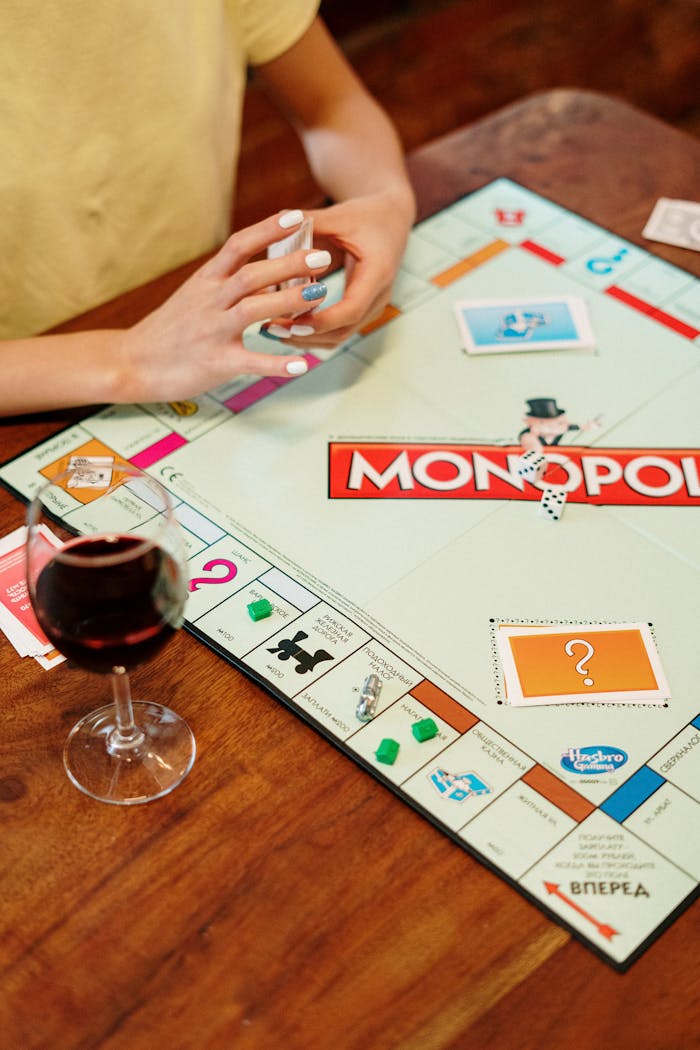A person playing Monopoly with a glass of wine on a wooden table.